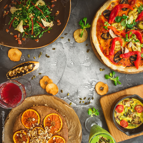 Food frame made of pizza with vegetables, salad, pie and fruit drinks on dark background. Flat lay, top view.