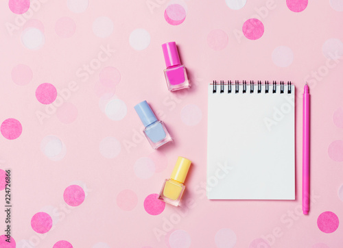 Empty note pad and colorful nail polishes on pink confetti background.