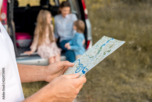 cropped shot of man holding map while his family sitting in car trunk in field © LIGHTFIELD STUDIOS