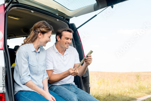 happy adult couple sitting in car trunk and looking at map while having car trip © LIGHTFIELD STUDIOS
