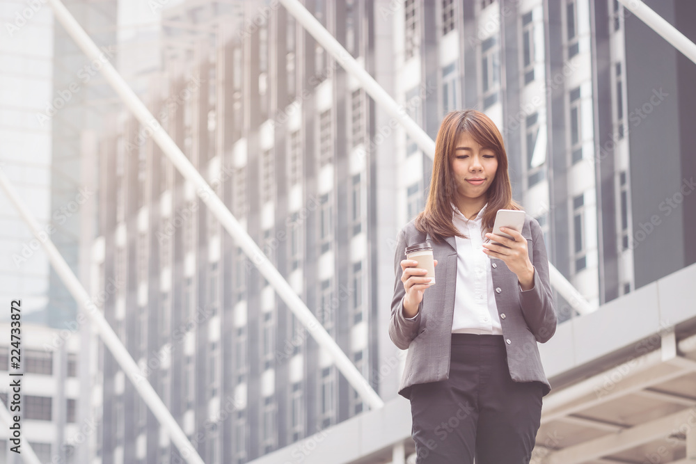 Businesswoman using smart phone and drinking hot coffee in the morning at ueban background Businesswoman using smart phone and drinking hot coffee in the morning at ueban background