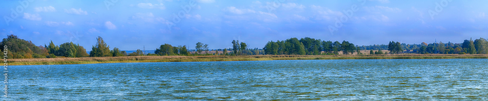 Panoramic shot of a beautiful summer countryside. River, forest and blue sky.