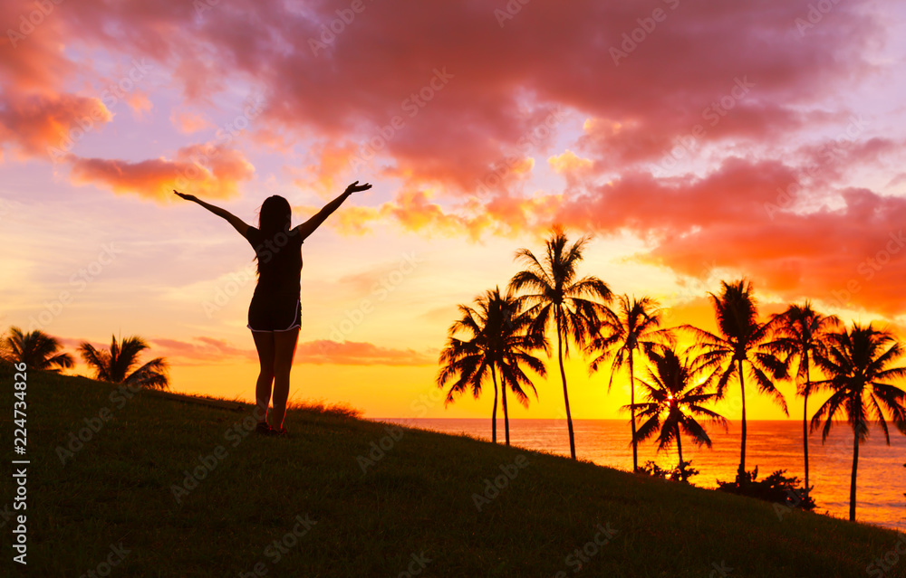 Happy female with arms up enjoying a beautiful tropical sunset. 