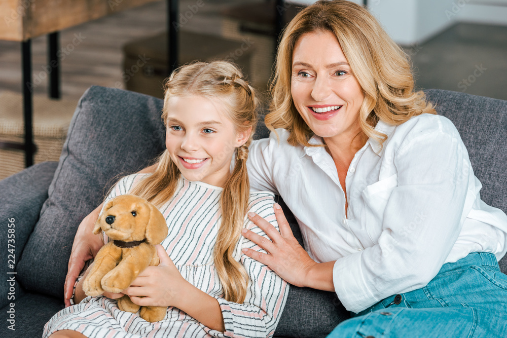 happy mother and daughter sitting on couch and looking away happy mother and daughter sitting on couch and looking away