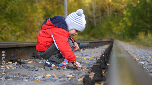 Lonely boy playing on the railroad tracks. Dangerous games and entertainment. Autumn warm day.
