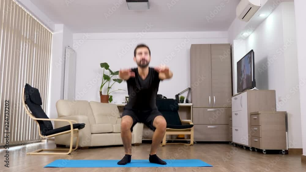 Young athletic man doing squats in the living room. Sport at home. Panning up Young athletic man doing squats in the living room. Sport at home. Panning up
