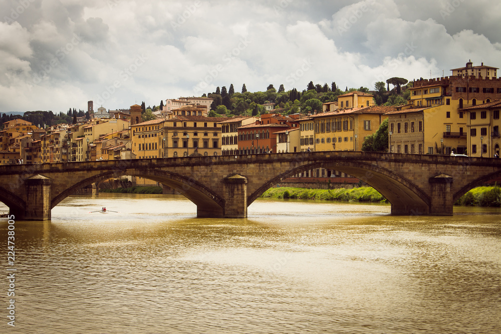 Panoramic view of the city of Florence. Storm clouds cover the sky. A small rowing boat circulates in the river.