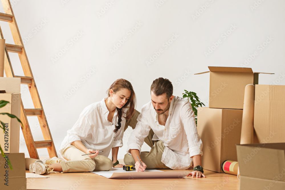Couple moving to a new home. Happy married people at new apartment. The family at repair and relocation planing to accommodation against boxes Couple moving to a new home. Happy married people at new apartment. The family at repair and relocation planing to accommodation against boxes