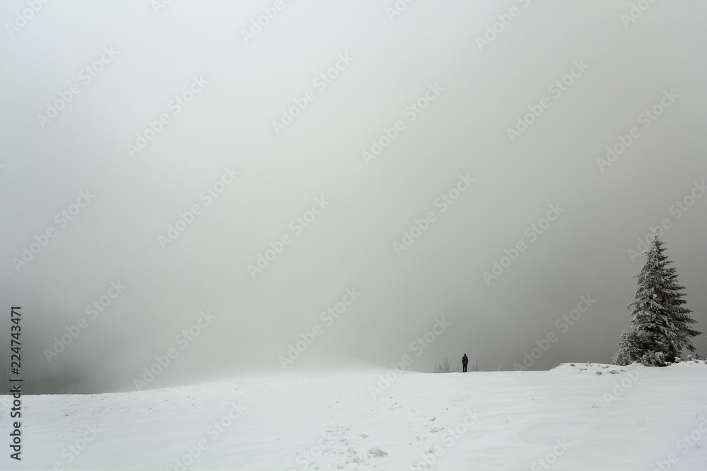 Fototapeta premium Far away lonely figure of a man standing outdoors in winter