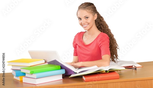 Friendly Girl Sitting Behind a Desk with a Books and Using