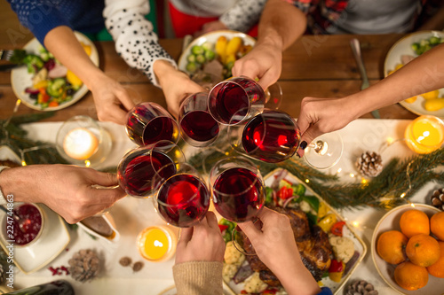 holidays and celebration concept - close up of friends having christmas dinner at home, drinking red wine and clinking glasses