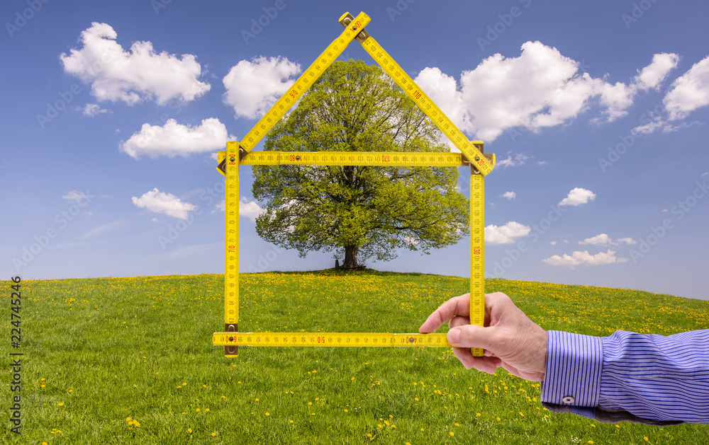 Makler hält Meterstab in Form von einem Haus als Symbol für Wohnen im Grünen Makler hält Meterstab in Form von einem Haus als Symbol für Wohnen im Grünen