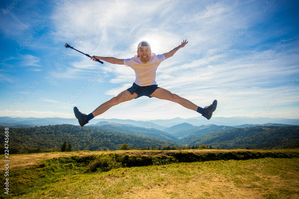 Summer hiking in mountains. Young tourist man in cap with hands up on top of mountains admires nature. Travel concept