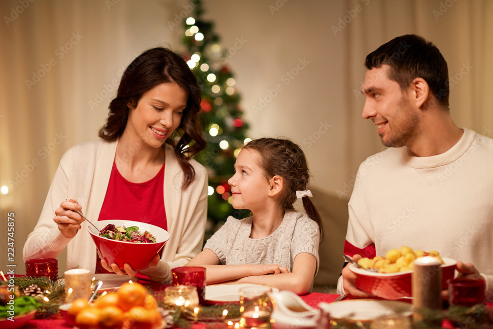 holidays, family and celebration concept - happy mother, father and little daughter having christmas dinner at home holidays, family and celebration concept - happy mother, father and little daughter having christmas dinner at home