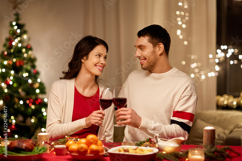 holidays  family and celebration concept - happy couple having christmas dinner at home and drinking red wine and clinking glasses