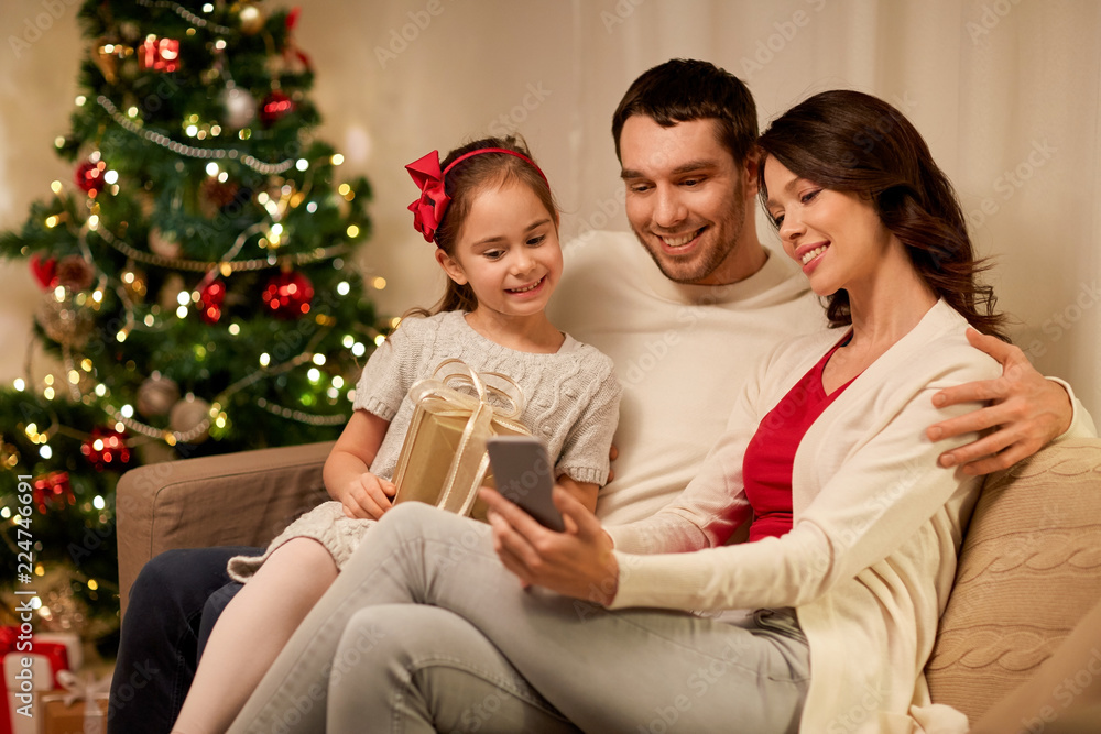 christmas, holidays and family concept - happy father, little daughter and mother with smartphone at home christmas, holidays and family concept - happy father, little daughter and mother with smartphone at home