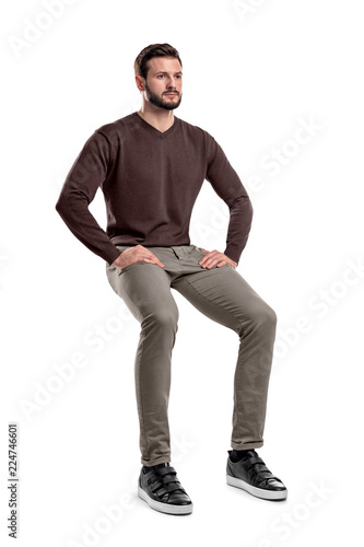 Canvas Print An isolated bearded man in casual wear sits on a white background with hands on his thighs