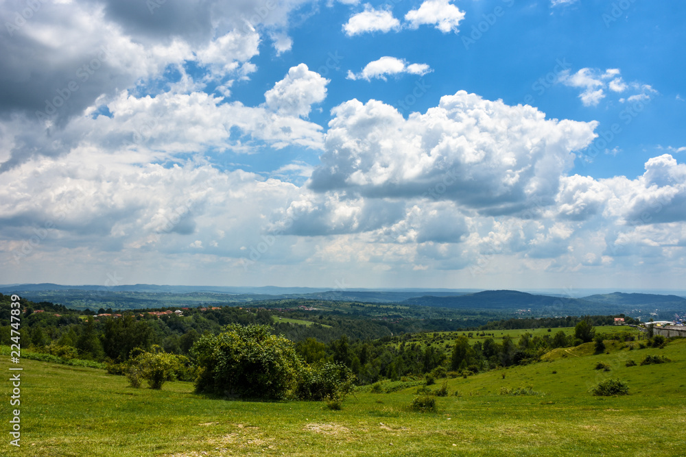 Landscape image of a green field with a cloudy but blue sky