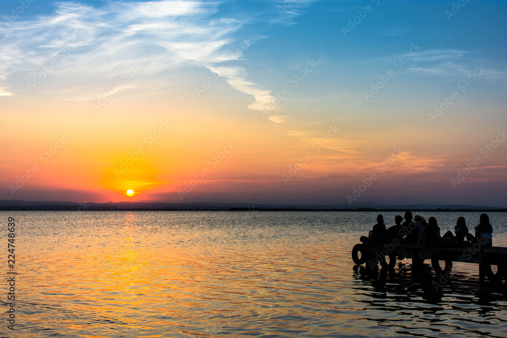 People sitting on a dock enjoying the summer sunset on a beautiful lake. Amazing sky in color 