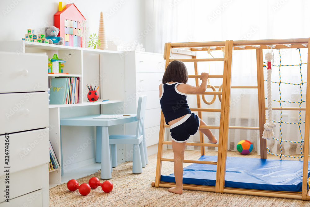 little girl performs gymnastic exercises on a wooden home sports ...