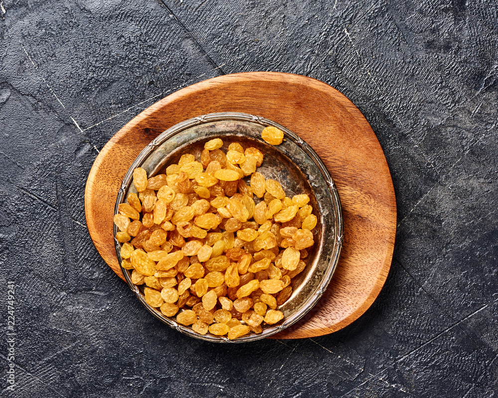 Fototapeta premium Yellow raisins on black concrete background. Top view of dried grapes.