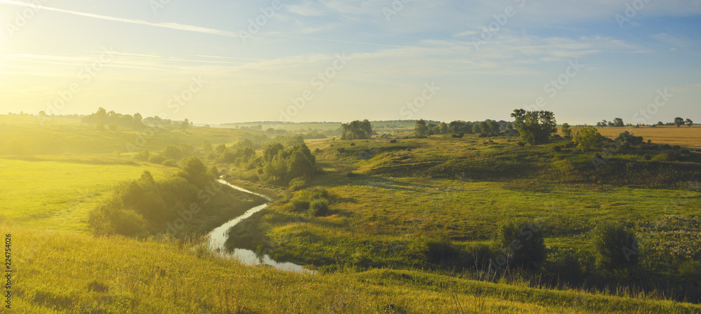 Obraz premium Sunny summer landscape with river flowing between the beautiful green hills,fields and meadows.