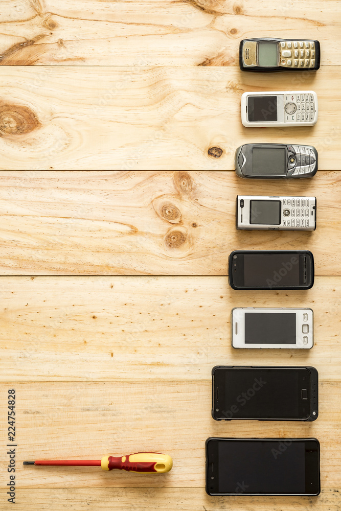 Several old and new mobile phones with screwdriver placed on wooden background Several old and new mobile phones with screwdriver placed on wooden background