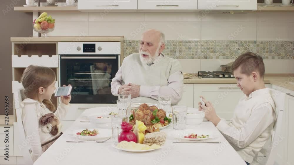 Grandpa Communicates With Grandchildren At The Table Before A Family Dinner Grandpa Communicates With Grandchildren At The Table Before A Family Dinner