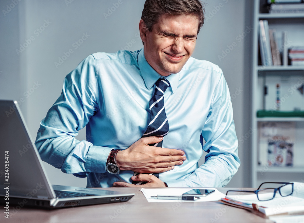 Employee suffers from severe pain in stomach. Photo of man working in the office. Medical concept. Employee suffers from severe pain in stomach. Photo of man working in the office. Medical concept.