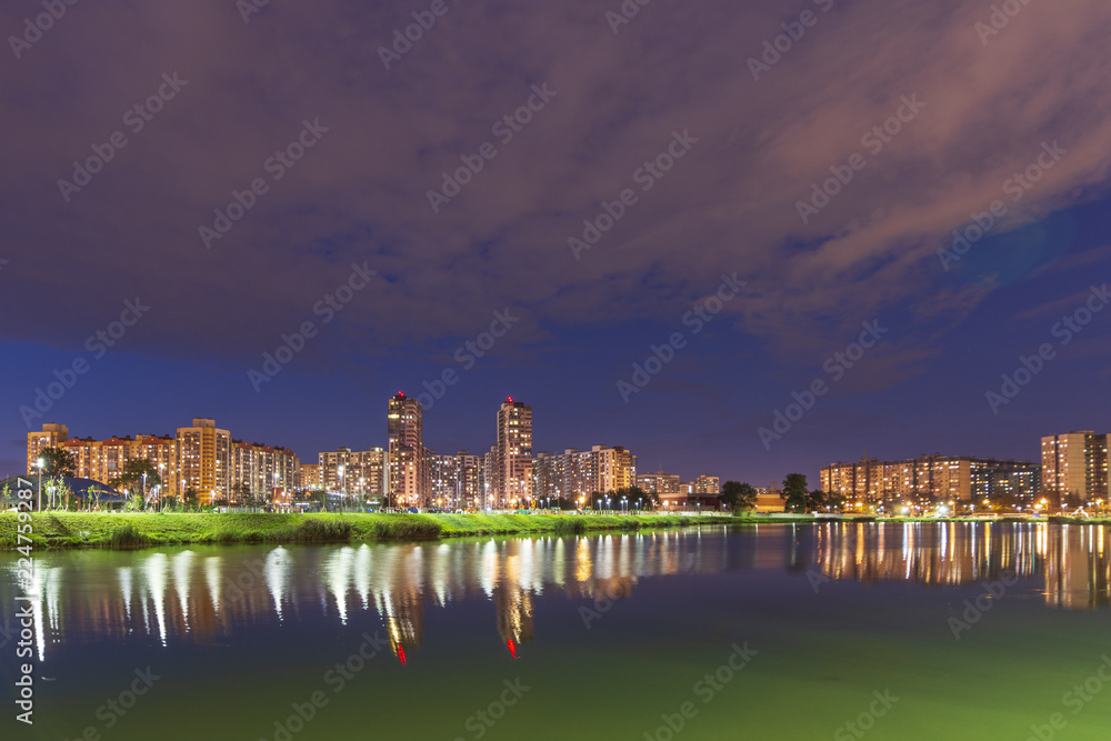 Night cityscape of residential buildings and park with a pond in the urban outskirts