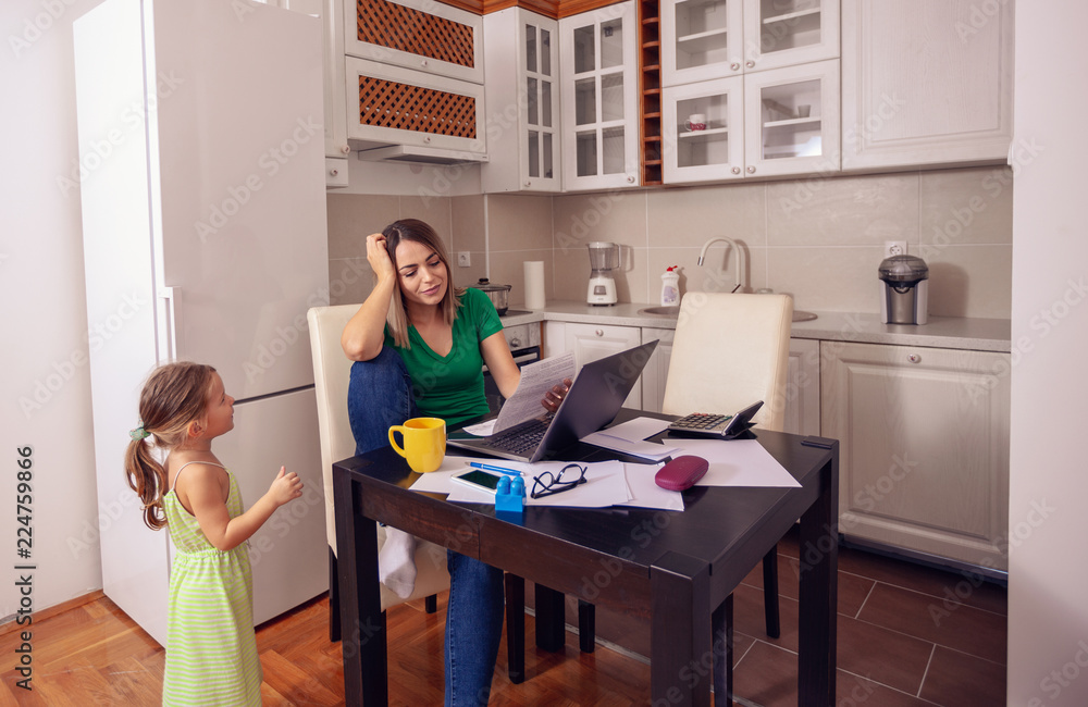 Smiling woman working from home with computer while looking after his daughter.. Smiling woman working from home with computer while looking after his daughter..
