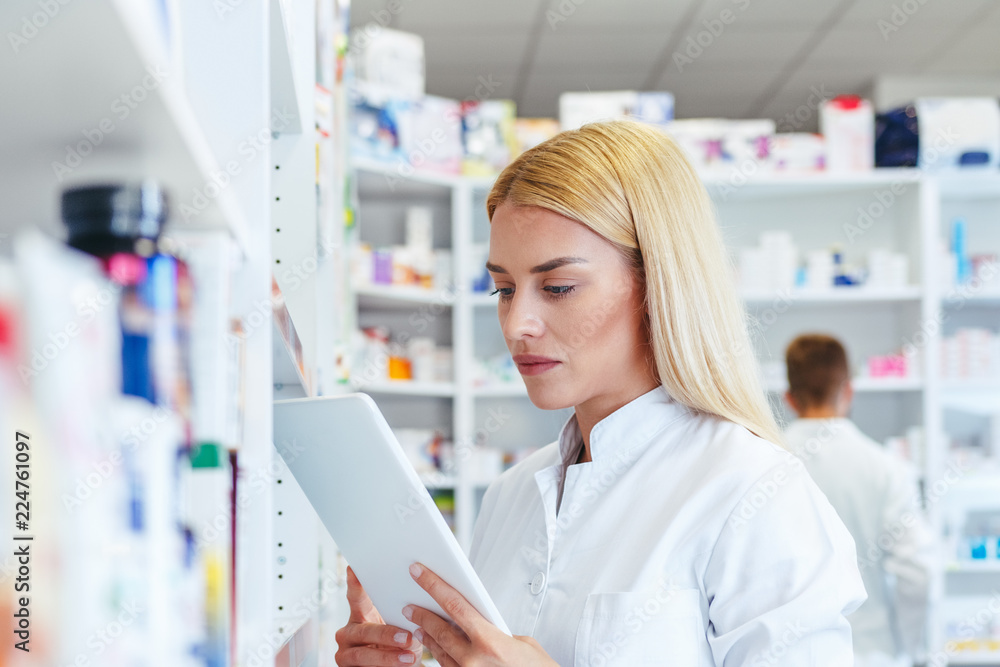 Woman pharmacist checking a medicine while holding a tablet in pharmacy drugstore