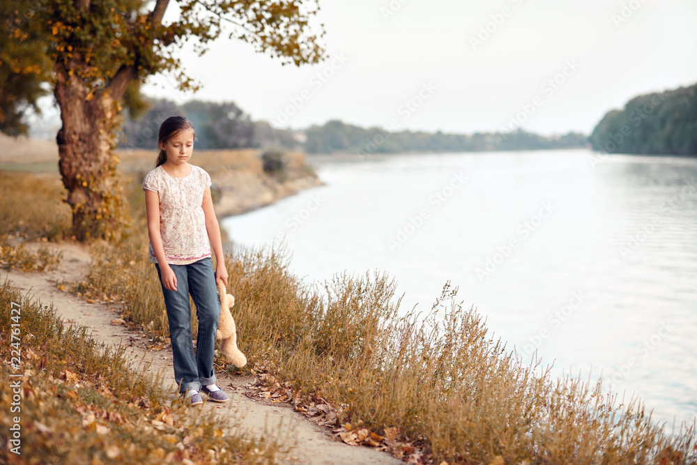 the girl child with toy bear walking along the path in the forest at sunset, beautiful river and landscape the girl child with toy bear walking along the path in the forest at sunset, beautiful river and landscape