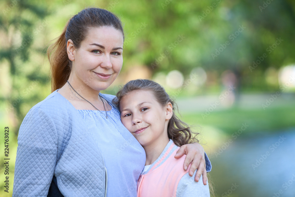 Portrait of Caucasian mother and daughter standing together, embracing in summer park Portrait of Caucasian mother and daughter standing together, embracing in summer park