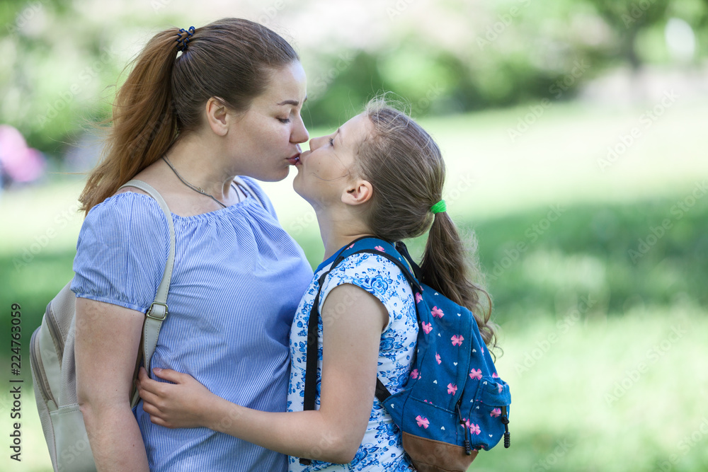 Mother kissing her daughter while walking summer park together