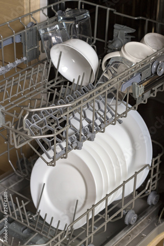 Open dishwasher with white big clean plates. cups and bowls inside