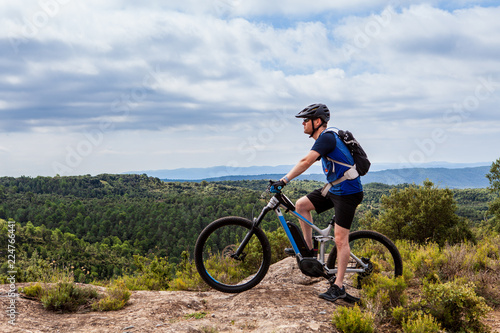Male mountain biker on ebike standing on top of a hill, looking left