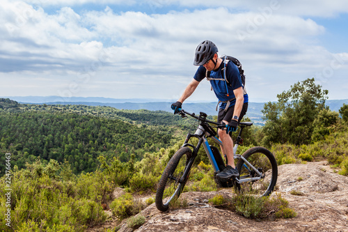 Male mountain biker balancing his ebike on a rock, nice landscape in the background
