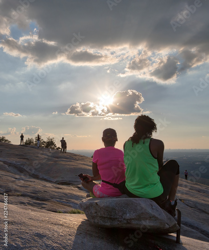 Unidentifiable hikers watching the sun begin to set from a rock at the top of Stone Mountain in Georgia on a bright summer day