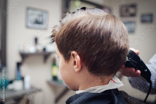 Hairdresser making a haircut to a boy with clipper.
