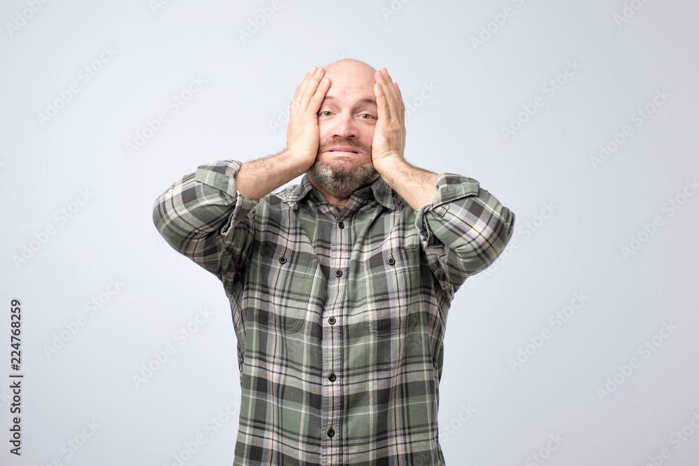 Mature annoyed man pulling skin on face with hands. He is scared or tired of stress. Mature annoyed man pulling skin on face with hands. He is scared or tired of stress.