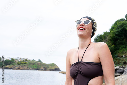 Portrait of a woman by the beach with a 1950's swim hat and sunglasses on posing on a rock