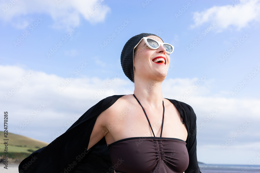 woman standing on the beach with a swimming costume on and 1950's swim hat and sunglasses woman standing on the beach with a swimming costume on and 1950's swim hat and sunglasses