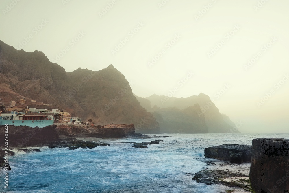 typical evening island scene with hazy dusty cliffs and the crystal clear blue sea with the buildings of a small village