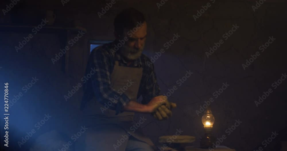 Portrait shot of the handsome old Caucasian man in the apron molding the clay in hands while having pottery manufacturing. Portrait shot of the handsome old Caucasian man in the apron molding the clay in hands while having pottery manufacturing.