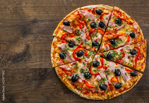 slices of Pizza with Mozzarella cheese, ham, pepper, meat, Tomatoes, olives, Spices and Fresh Basil. Italian pizza on wooden background