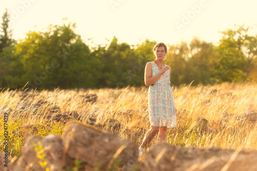 Beautiful woman in a summer dress on a summer evening in the ruins of Ismatorp, a prehistoric ring fort on the swedish island of Öland. Backlite photograph, warm light nordic summer.