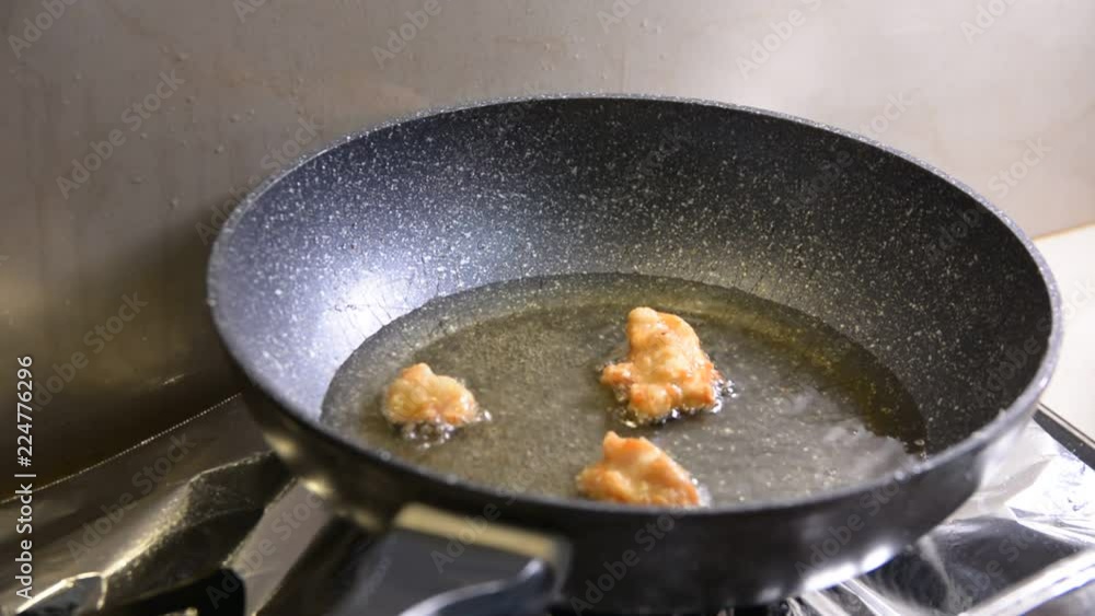 breaded chicken pieces being deep fried in a cast iron pan breaded chicken pieces being deep fried in a cast iron pan