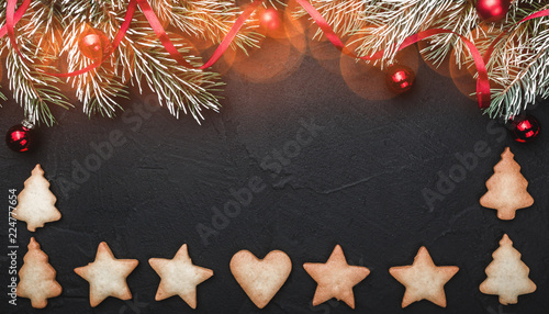 Black stone background  with fir branches adorned with red balls. Biscuits of various shapes. Top view. Effect of lights