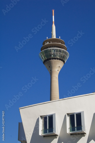 Fernsehturm in Düsseldorf vor blauem Himmel und einem modernen Gebäude